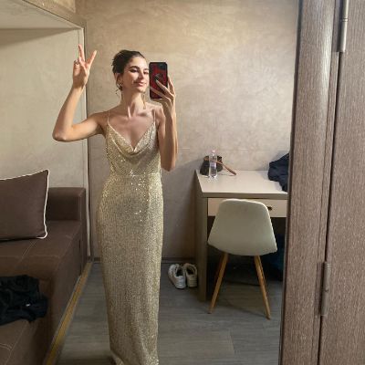 Mia Challis taking a mirror selfie wearing a gold dress.